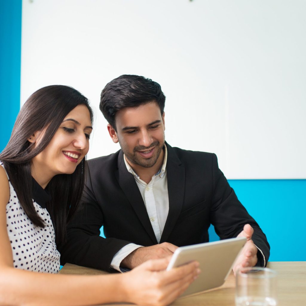 Portrait of happy young colleagues using digital tablet. Young Caucasian businessman and businesswoman sitting at table and watching data on pc tablet. Wireless technology in business
